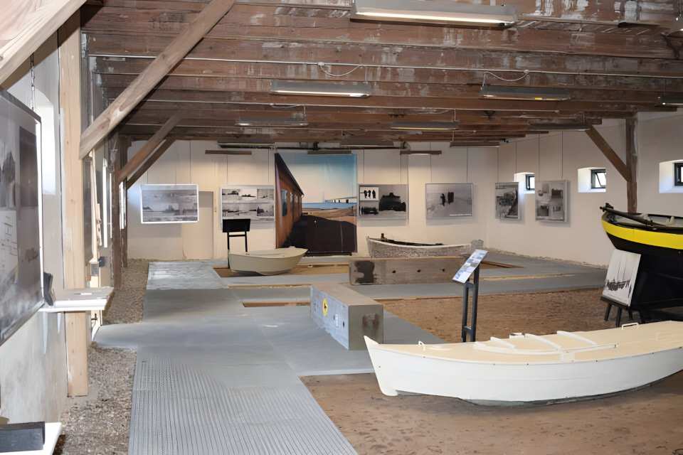 Indoor maritime museum exhibit with several boats and historical photos on white walls.