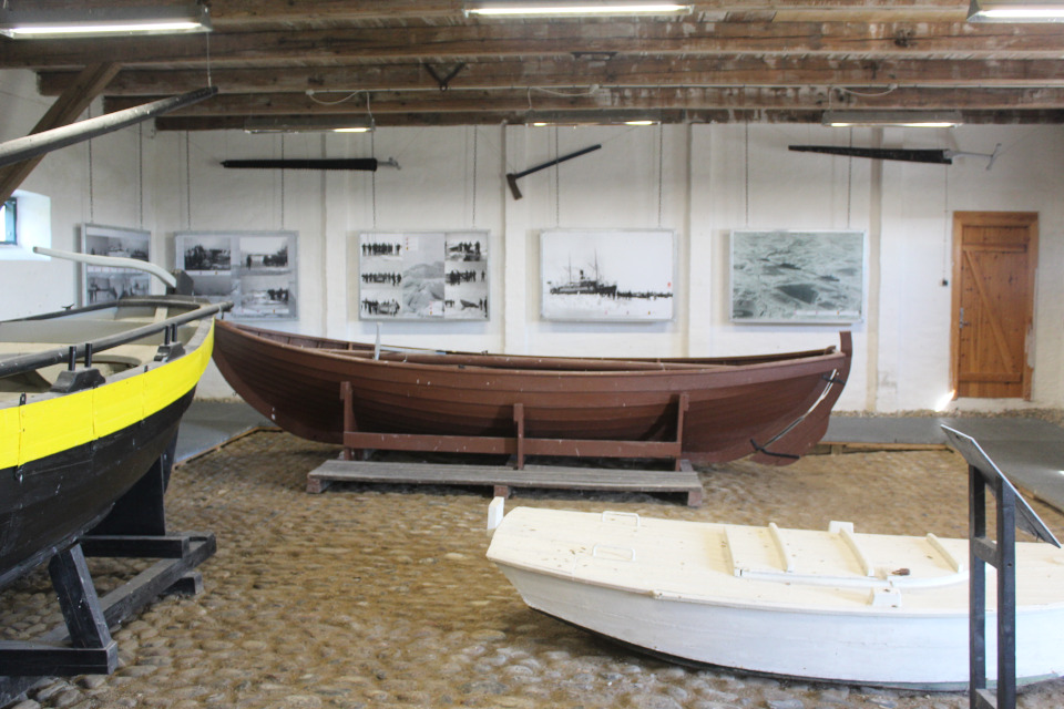 Indoor boat museum with three boats on display and historical photos on the back wall.